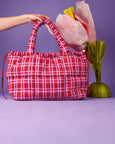 Red plaid bag held by a hand with tulips on a purple background