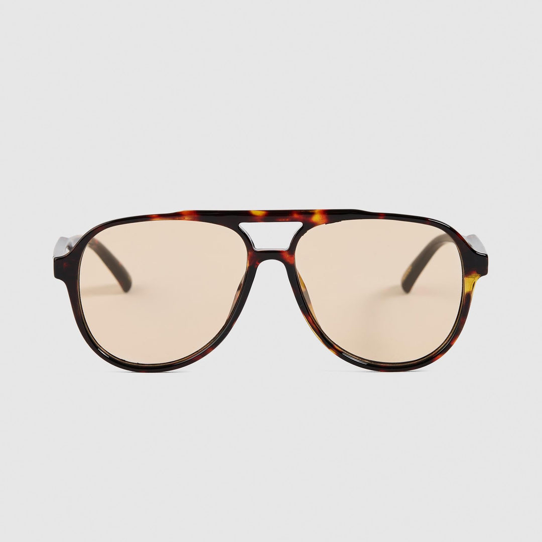 A pair of aviator-style sunglasses with a dark brown and amber tortoiseshell frame and light beige lenses, shown against a solid light gray background.