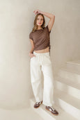 Woman in a brown top and white pants standing on a staircase with a neutral background