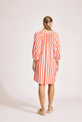 Woman wearing a red and white eb and ive striped dress on a light pink background