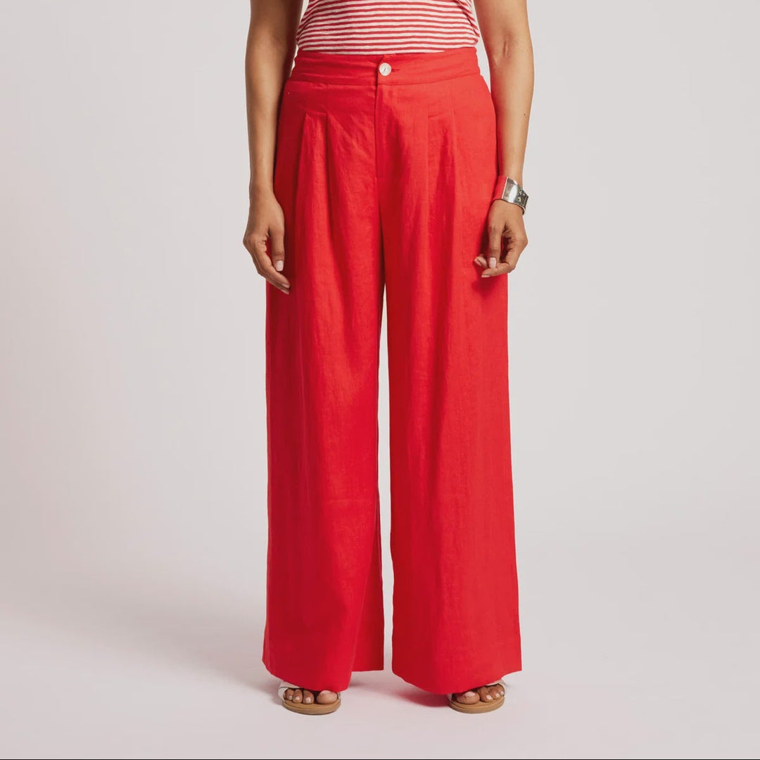 A woman modeling a red and white striped tank top paired with bright red wide-leg trousers, standing against a light gray studio background.