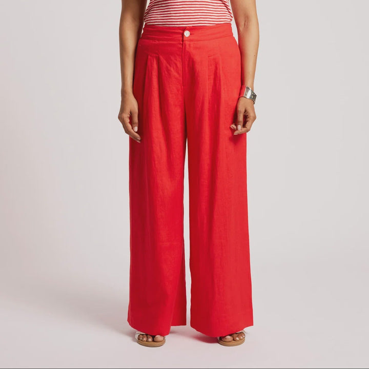 A woman modeling a red and white striped tank top paired with bright red wide-leg trousers, standing against a light gray studio background.