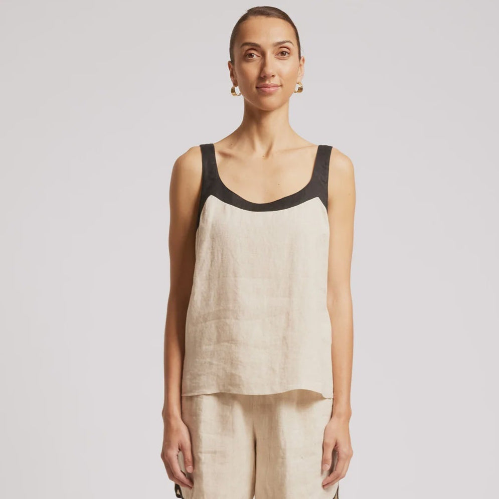 A woman modeling a sleeveless linen-look top and matching shorts set in a light beige/cream color with black trim, paired with dark sandals, against a plain light gray studio background.