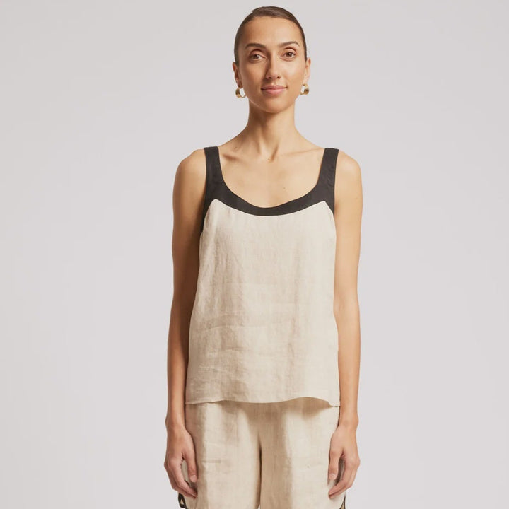 A woman modeling a sleeveless linen-look top and matching shorts set in a light beige/cream color with black trim, paired with dark sandals, against a plain light gray studio background.