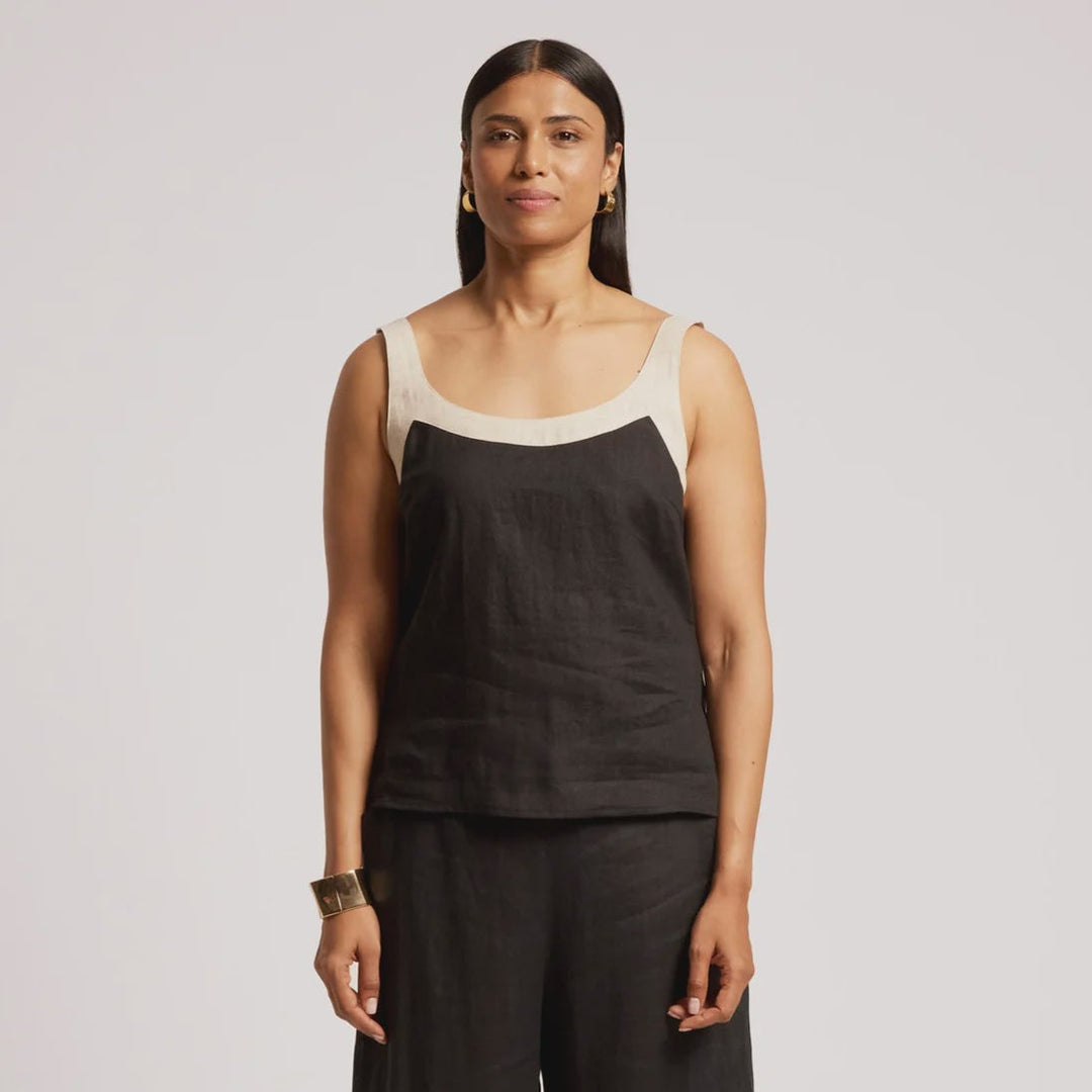 A woman modeling a black sleeveless top and matching wide-leg pants set against a light gray studio background.