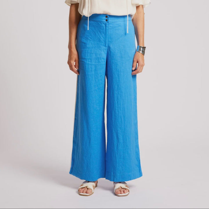 A woman modeling a white short-sleeve tie-front top and bright blue wide-leg pants against a light gray studio background.
