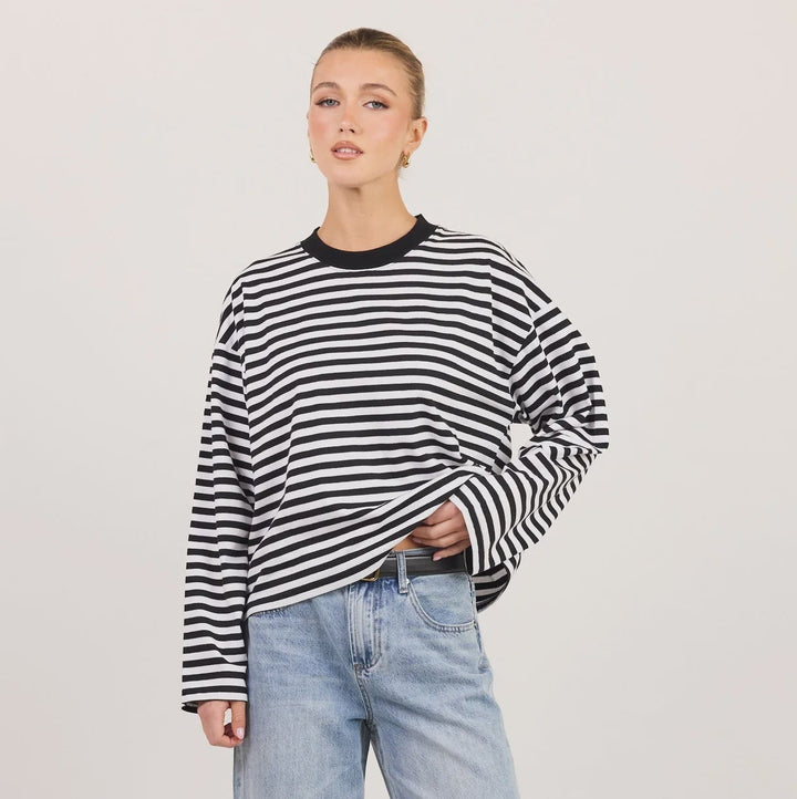 A model wearing a black and white striped long-sleeve top, light-wash wide-leg jeans, and black sandals, standing against a plain off-white studio background.
