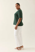Woman wearing a green knitted isle of mine top and white pants on a plain background