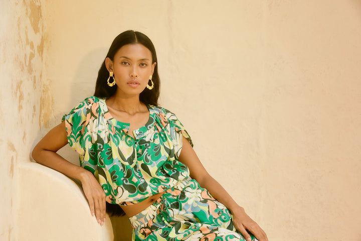 Woman wearing a green floral isle of mine outfit sitting against a beige wall.