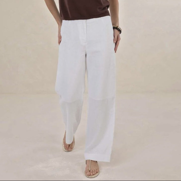 Woman wearing a brown sleeveless top and white pants against a beige background