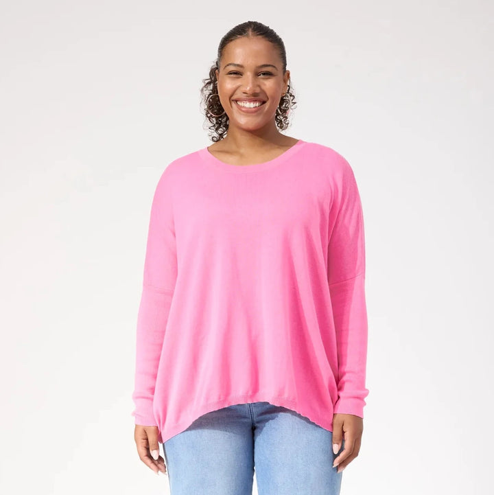 Woman wearing a bright pink top and light blue jeans on a white background