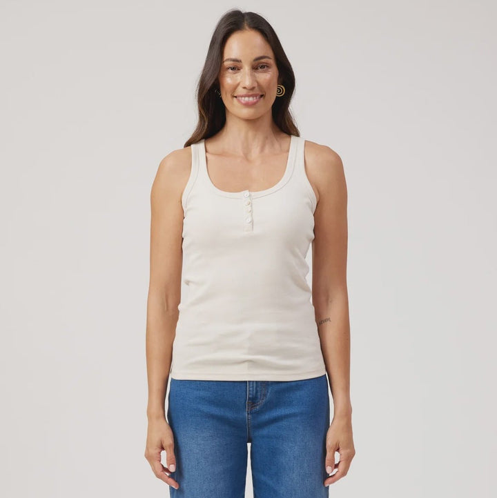 A woman modeling a white ribbed tank top and blue wide-leg jeans against a plain light gray studio background.