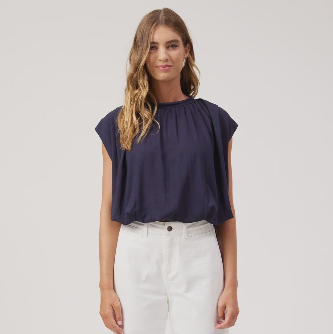 A woman modeling a navy blue short-sleeve top and white wide-leg trousers against a plain white studio background.