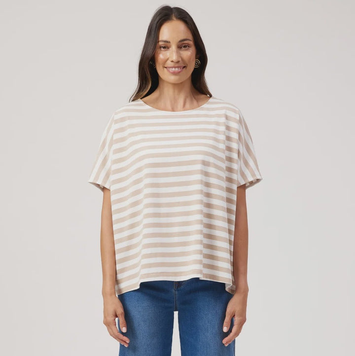 A woman modeling a short-sleeve top with horizontal cream and beige stripes, paired with wide-leg blue jeans and brown sandals, against a light gray studio background.