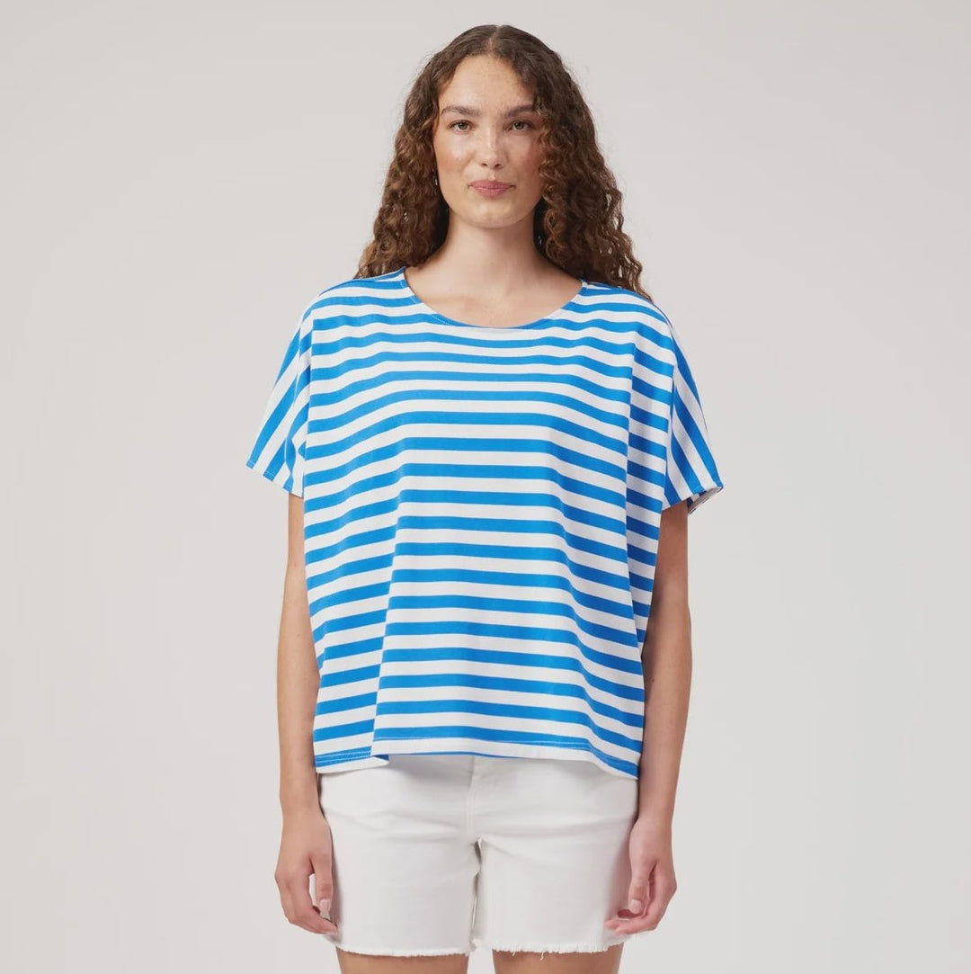 A woman modeling a blue and white striped short-sleeve top with white shorts, standing against a light gray studio background.