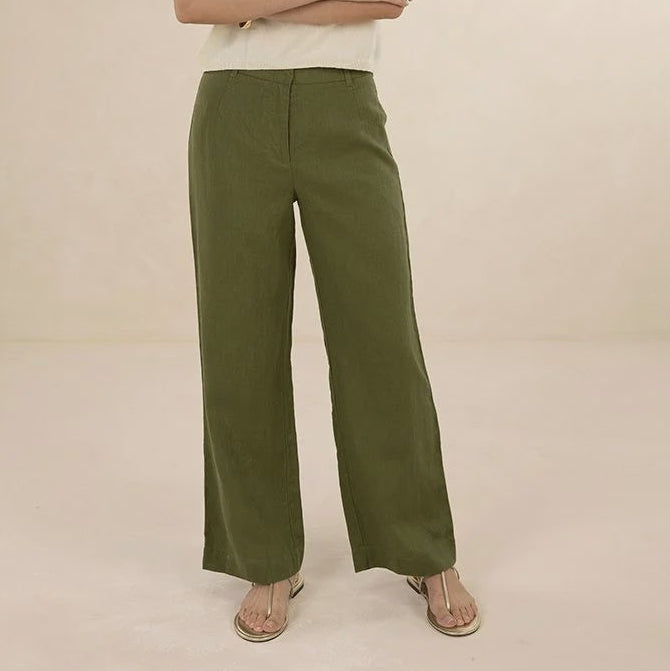 A woman modeling a sleeveless cream top and olive green wide-leg pants against a plain beige studio background.