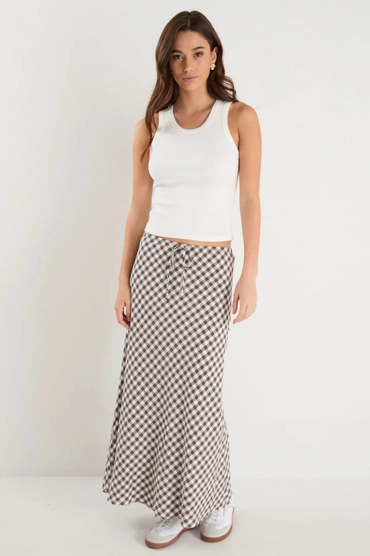 Woman wearing a white sleeveless top and a long gingham skirt on a plain background