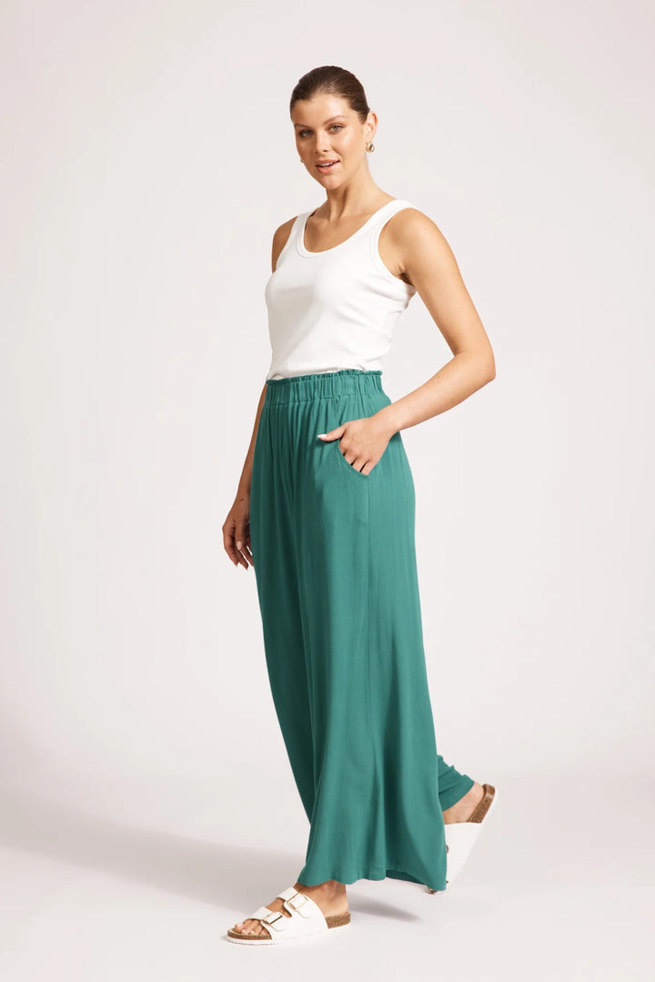 Woman wearing a white top and teal Eb & ive pants on a white background