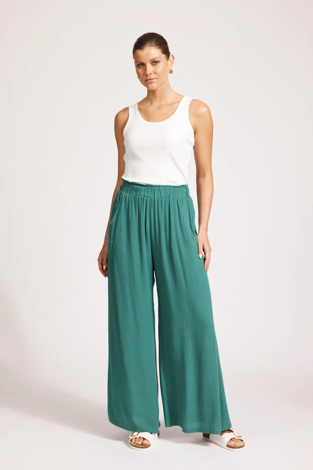 Woman wearing a white sleeveless top and Eb & Ive teal wide-leg pants on a white background