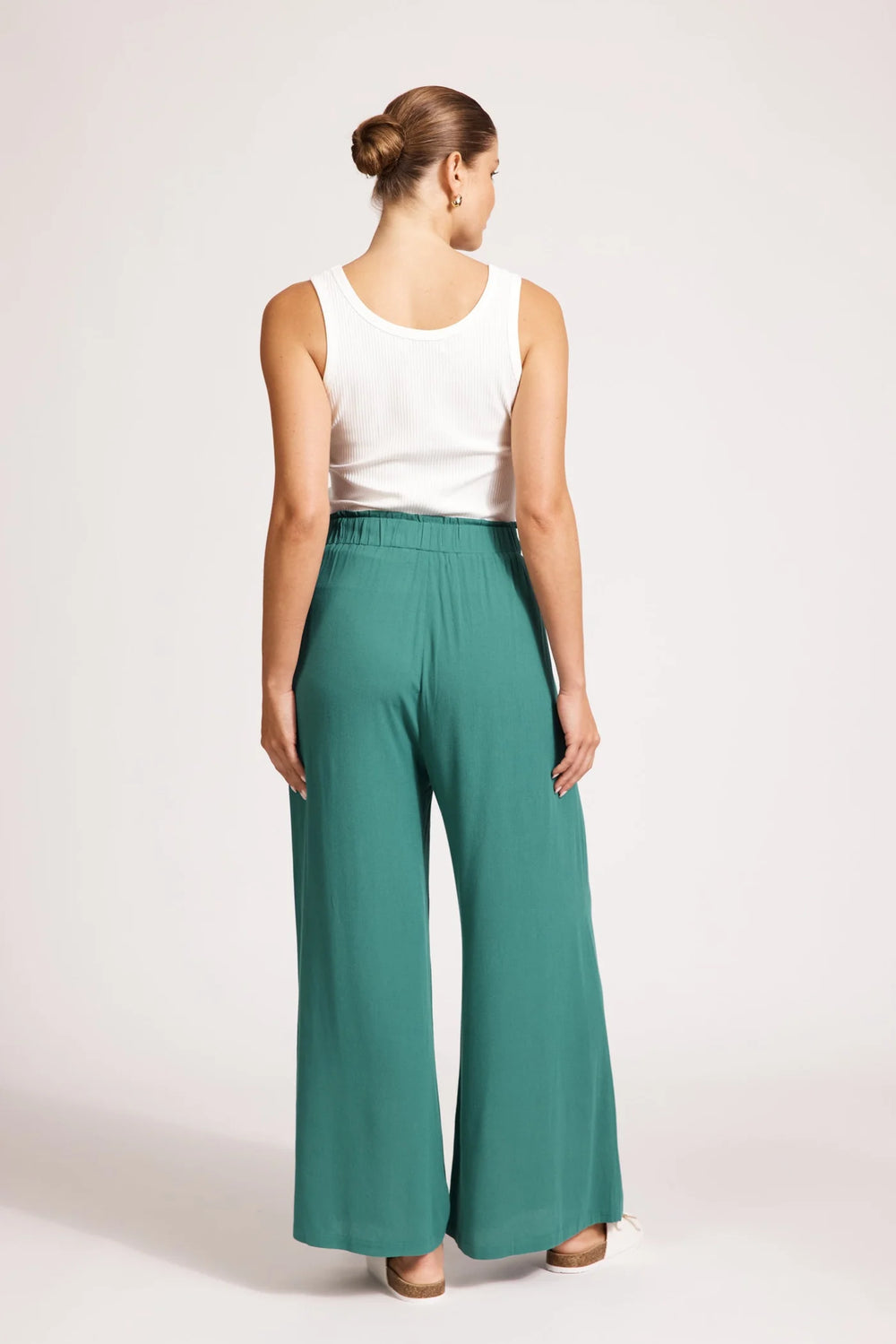 Woman wearing teal Eb & ive pants and a white top on a plain background