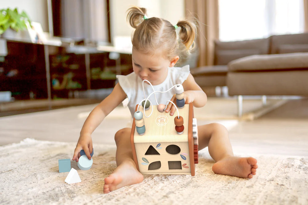 Child playing with a wooden shape sorter toy on a carpeted floor.