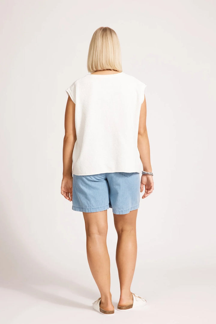 Woman wearing a white t-shirt and light blue shorts on a plain background