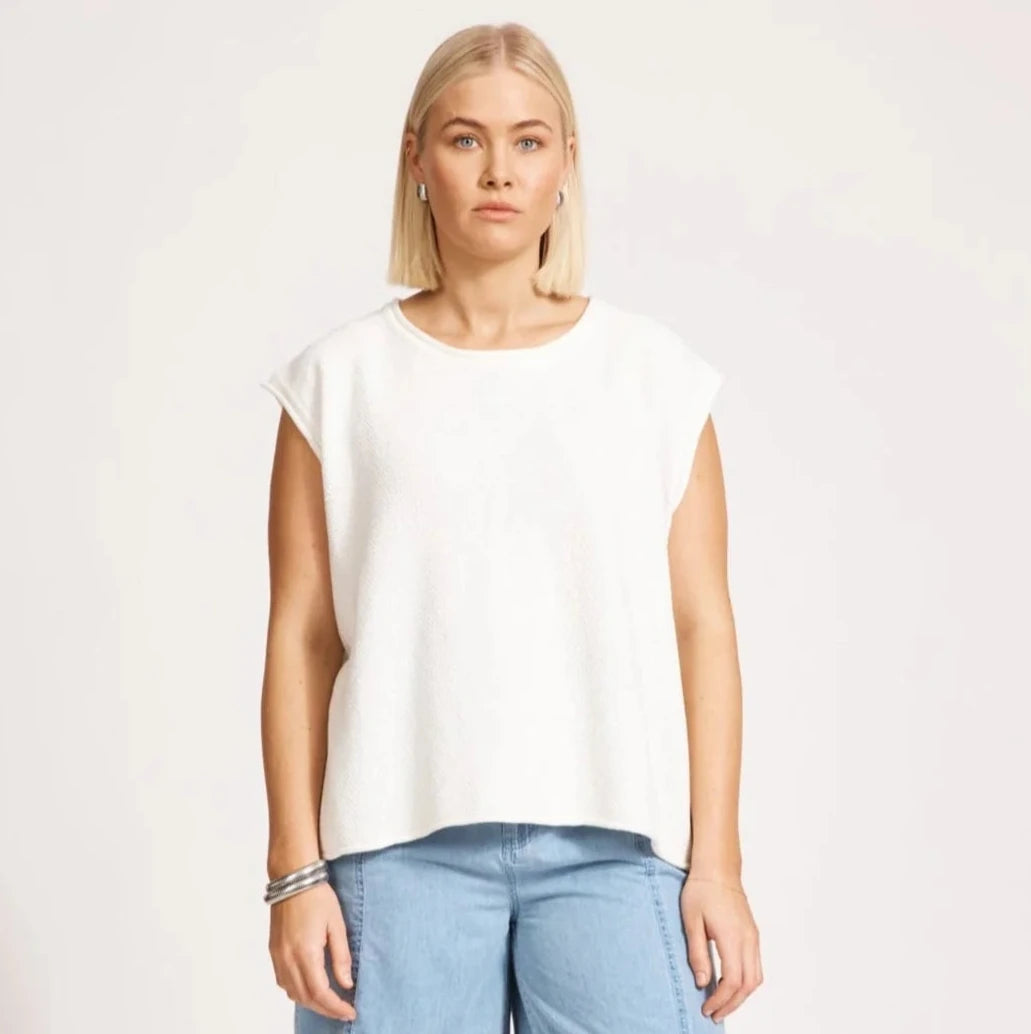 Woman wearing a white top and blue shorts on a plain background