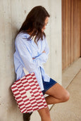 Woman holding a red and white checkered bag against a concrete wall.