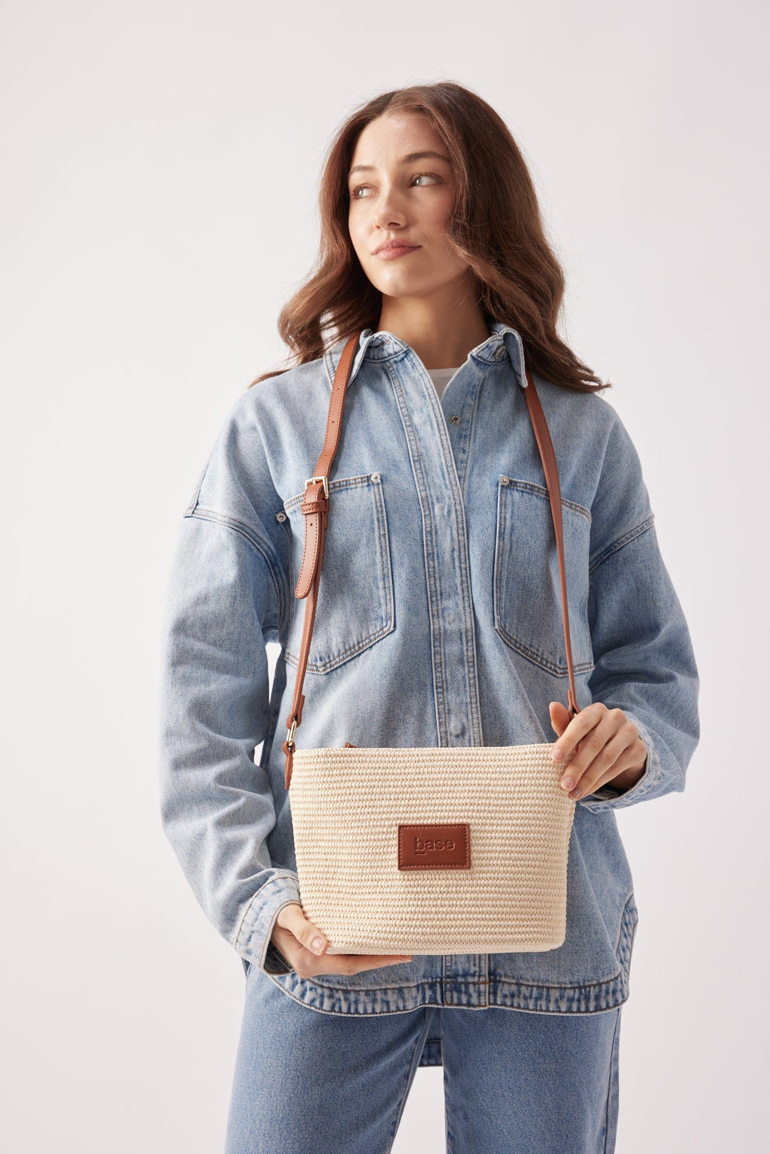 Woman holding a beige woven handbag with a brown strap against a white background