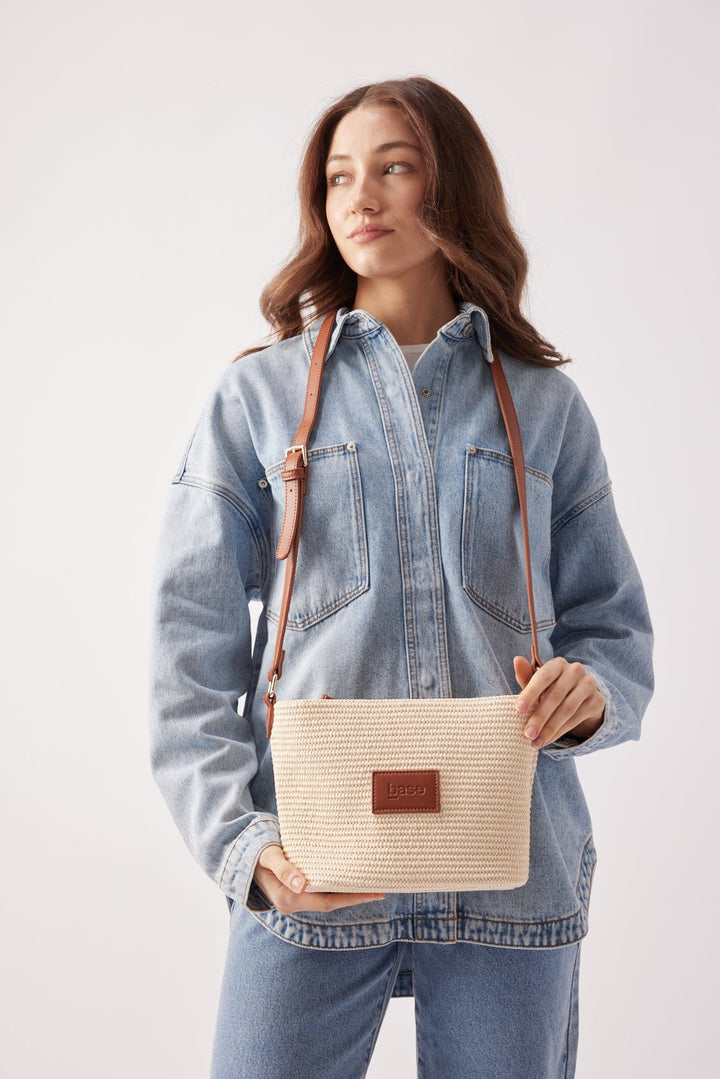 Woman holding a beige woven handbag with a brown strap against a white background