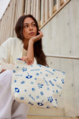 Woman holding a white tote bag with blue patterns against a neutral background
