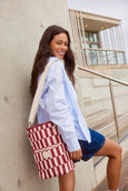 Woman holding a red and white checkered base cooler bag against a building.