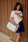 Woman holding a white bag with blue patterns against a wooden wall