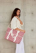 Woman holding a red and white patterned cooler bag against a concrete wall