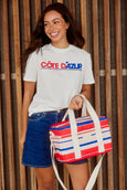 Woman holding a red, white, and blue bag wearing a 'Côte Dázur' t-shirt against a wooden background