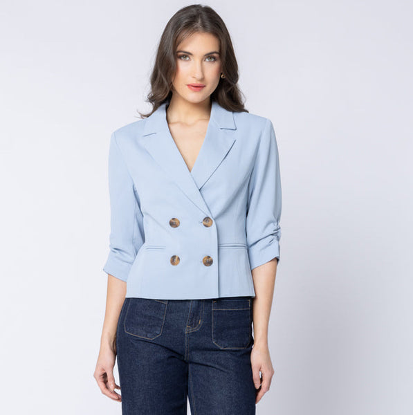 Woman wearing a light blue billie the label blazer and dark blue jeans on a white background