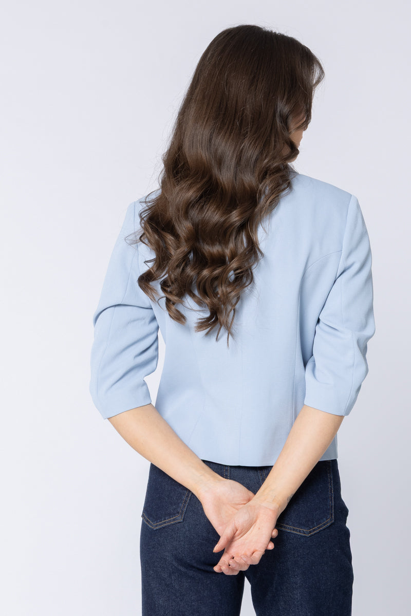 Person wearing a light blue billie the label blazer and dark jeans with long, wavy hair on a plain background