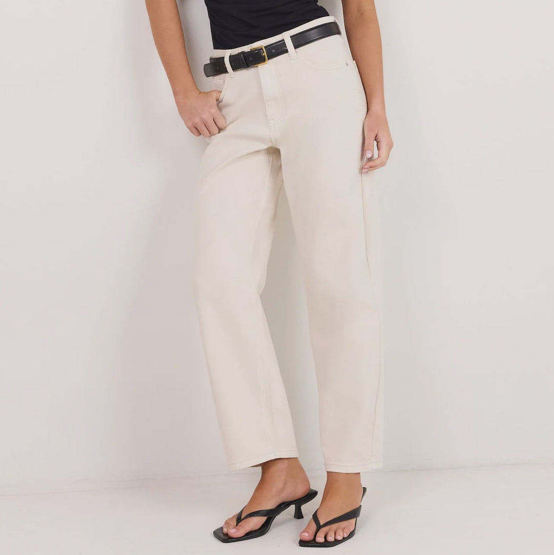 A woman modeling a black off-the-shoulder top and cream wide-leg trousers with a black belt, standing against a plain white studio background.