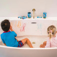 Two children sitting in a bathtub with crayon drawings on the wall.