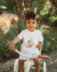 Child sitting on a tricycle outdoors with greenery in the background