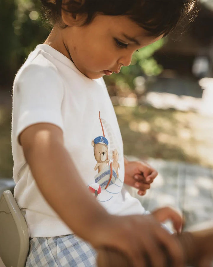 Child wearing a white Bebe shirt with a teddy bear graphic outdoors