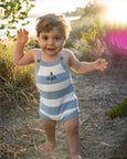 Child wearing a Bebe blue and white striped romper standing outdoors with natural light.