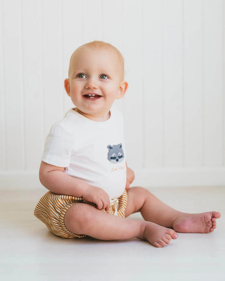 Baby sitting on a white surface wearing a Bebe white onesie with a bear design and gold bloomers.