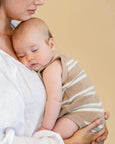 Baby wrapped in a striped blanket being held by a person against a beige background