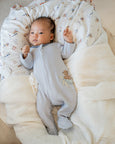 Baby in a gray Bebe onesie with animal designs lying on a soft, patterned blanket.