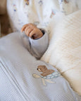 Close-up of a baby's hand reaching towards a soft textured blanket with a teddy bear design.