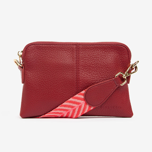 Red handbag with a pink and white patterned strap on a white background