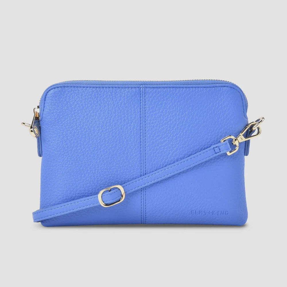 A bright blue textured leather crossbody bag with a matching adjustable strap and gold-tone hardware, shown against a light gray background.