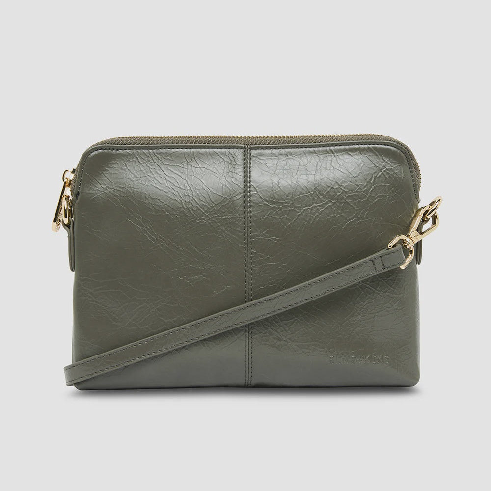 An olive green faux-leather crossbody bag with a top zipper and a matching shoulder strap, accented with gold-tone hardware, shown against a light gray background.