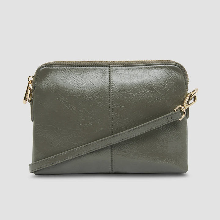 An olive green faux-leather crossbody bag with a top zipper and a matching shoulder strap, accented with gold-tone hardware, shown against a light gray background.